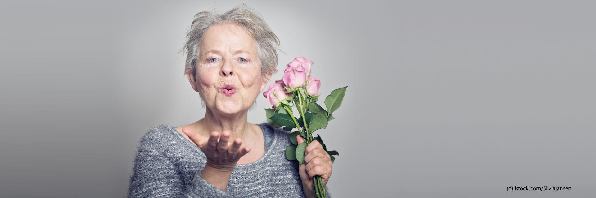 Seniorin hält einen Rosenstrauß in der Hand und schickt einen Luftkuss