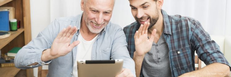 Ein älterer und ein jüngerer Mann schauen in ein Tablet und winken