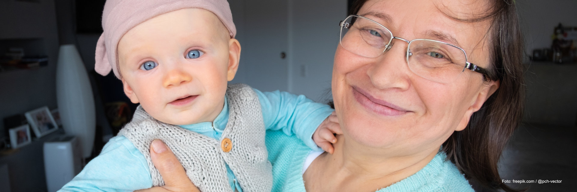 Eine Seniorin hält ein Baby im Arm, beide lachen in die Kamera.