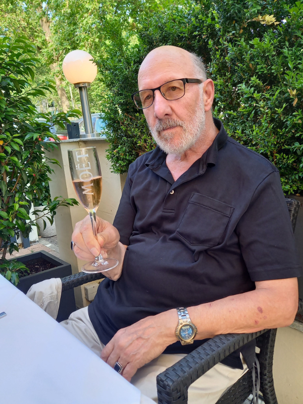 Ein Mann sitzt im Freien an einem Tisch und erhebt ein Glas
